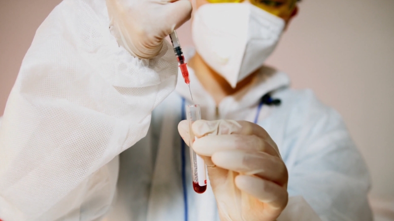 Medicinski radnik u zaštitnoj opremi ubrizgava krv u epruvetu tokom laboratorijske analize