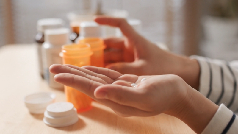 Osoba u jednoj ruci drži lekove, a u drugoj bočicu