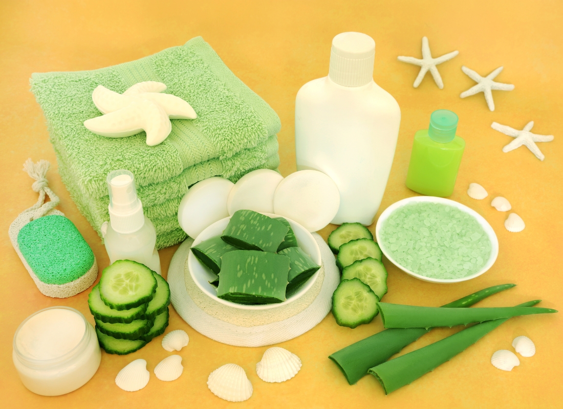 prikaz prirodnih preparata za kožu nakon sunčanja, aloe vera, krastavac, kremice, i peškir na narandžastoj pozadini