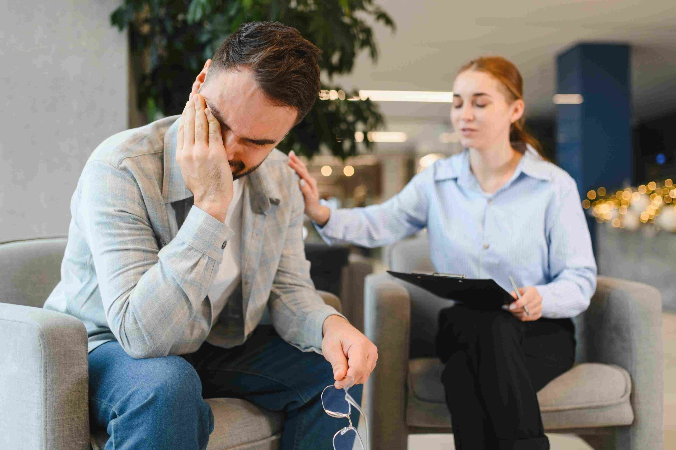 Osoba sedi uznemireno i drži glavu rukom, dok terapeut pored nje pruža podršku tokom razgovora