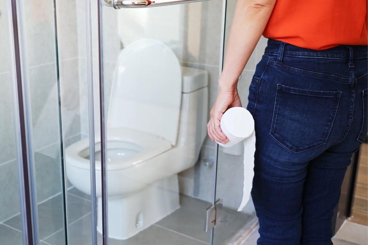 devojka stoji ispre wc šolje i drži toalet papir u ruci