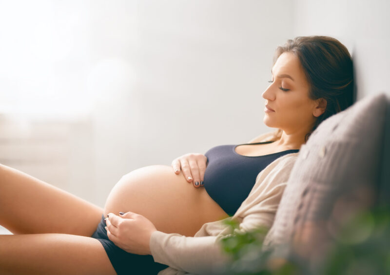 Buduća mama tokom trudnoće odmara i drži ruke na stomaku